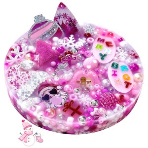 Puede incluir: Una pieza circular de resina rellena con dijes navideños en rosa, blanco y plata, incluyendo una cara de Santa, un hombre de jengibre, copos de nieve y adornos. Dos placas ovaladas presentan el texto MERRY y BRIGHT en letras coloridas.