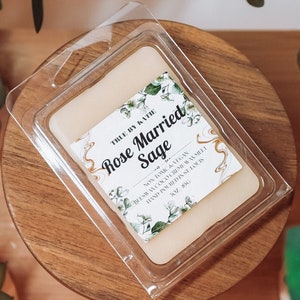 May include: A clear wax melt container with a white wax melt inside. The label reads "The Ivy & Lily Rose Married Sage Soy Wax Melts Hand Poured &  Hand Blended Net Wt. 0.8 oz."