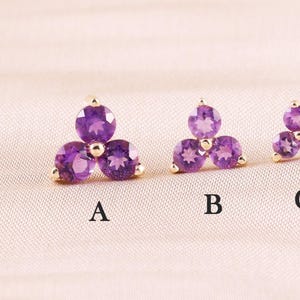 May include: Four gold stud earrings, each featuring three round purple amethyst stones arranged in a triangular cluster. The earrings are labeled A, B, C, and D, showing a progression in size from the largest at A to the smallest at D.