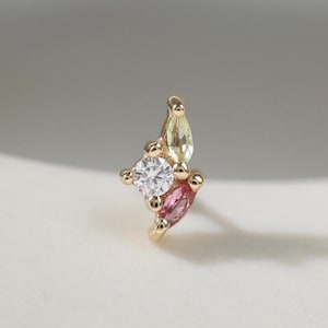 May include: A gold stud earring featuring a central round clear gemstone flanked by a marquise-cut yellow gemstone at the top and a marquise-cut pink gemstone at the bottom, all set in a delicate gold metal frame with a post backing.