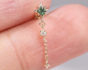 May include: A gold-colored earring featuring a star-shaped green gemstone at the top, with a delicate chain suspending a small diamond and a tiny star charm. The earring is designed for a single ear piercing.