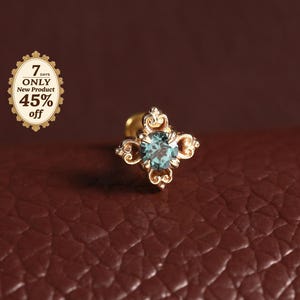 Puede incluir: Un pendiente de botón dorado con una piedra preciosa redonda de color azul claro en el centro, engastada en un marco de metal ornamentado de cuatro puntas. A la izquierda, una pequeña insignia ovalada muestra el texto 7 DAYS ONLY New Product 45% off.