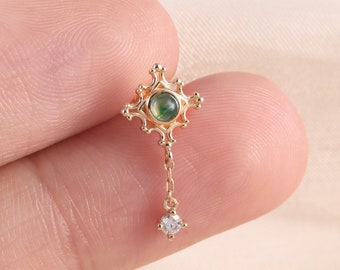 May include: Gold earring with a green stone and a small diamond dangling from a chain.