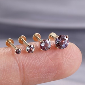May include: Four gold-toned stud earrings with round, faceted, color-changing stones that shift between purple and teal hues. Each earring features a thin metal post and a small, circular setting holding the gemstone securely in place.
