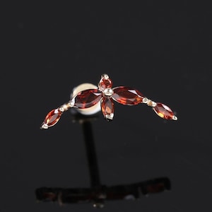 May include: A silver-toned earring with a floral design. The earring features a cluster of five marquise-cut, deep red gemstones at the center, with three additional gemstones extending outward on each side. The earring is set against a dark background.
