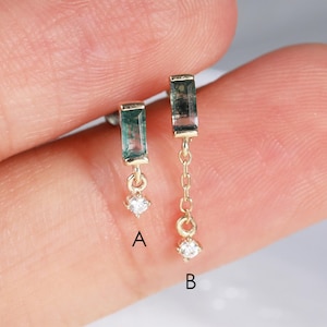 May include: Two gold earrings featuring rectangular green gemstones. Earring A has a single green baguette stone with a small round white stone dangling below. Earring B features a green baguette stone connected to a chain with a round white stone.