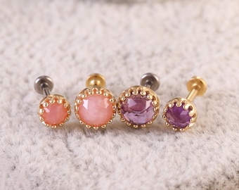 May include: Four small jeweled body piercing studs. Two are pink and two are purple. Each stud has a gold-colored setting with a beaded edge.