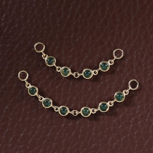 Puede incluir: Dos conectores de joyería dorados y curvos con pequeñas piedras cabujón redondas de color verde oscuro engastadas en metal. Cada pieza está unida por delicadas cadenas doradas y termina en un anillo de salto circular en ambos extremos.
