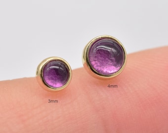 May include: Two gold-toned round gemstone earrings with purple stones. The earring on the left is 3mm in diameter and the earring on the right is 4mm in diameter.