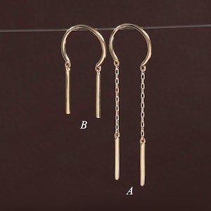 May include: Two gold-toned earrings suspended from a thin horizontal line. Earring B features a simple U-shaped wire with two short, solid bars. Earring A features a U-shaped wire with two longer, delicate link chains ending in solid bars.