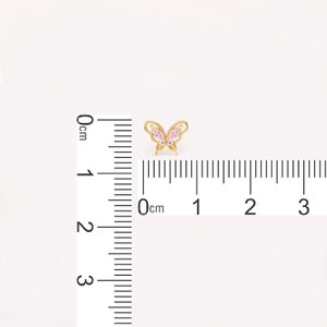 May include: A gold butterfly charm with pink and clear crystal accents. The charm is approximately 1 cm wide.
