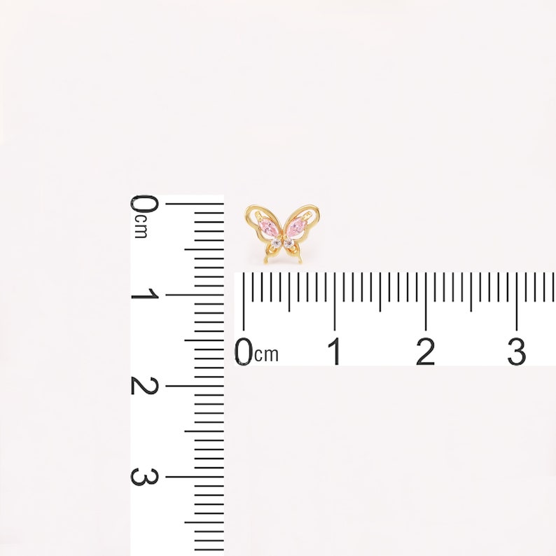 May include: A gold butterfly charm with pink and clear crystal accents. The charm is approximately 1 cm wide.