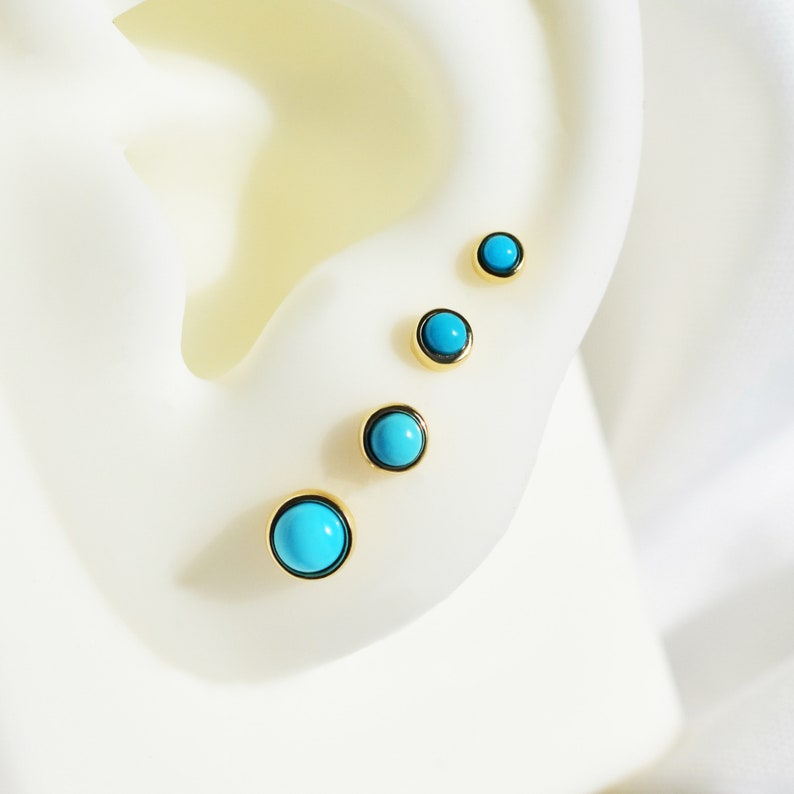 May include: Four turquoise gemstone earrings with gold settings, arranged in a line on a white surface.