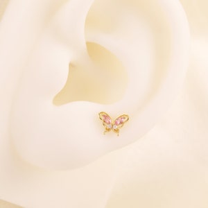 May include: A gold butterfly earring with pink and clear gemstones.