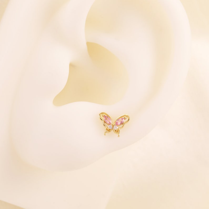 May include: A gold butterfly earring with pink and clear gemstones.