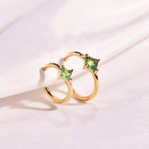 May include: A pair of gold hoop earrings with a square green stone set in each hoop.