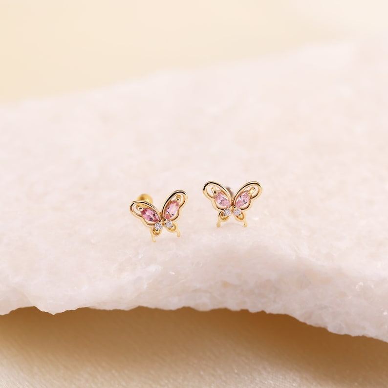 May include: A pair of gold butterfly earrings with pink and clear gemstones.