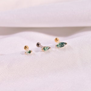 K&ouml;nnte beinhalten: Drei Ohrstecker mit einem gr&uuml;nen Stein in Marquiseform. Zwei sind goldfarben, einer silberfarben. Die Ohrringe werden auf einer wei&szlig;en, strukturierten Oberfl&auml;che pr&auml;sentiert. Jeder Ohrring hat einen Stecker und einen flachen R&uuml;cken.