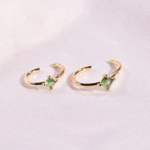 May include: A pair of gold ear cuffs with small square green gemstones.