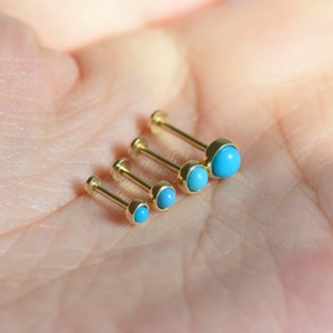 May include: Four gold body jewelry pieces with turquoise stones. The stones are different sizes, with the largest stone at the top of the image and the smallest stone at the bottom.