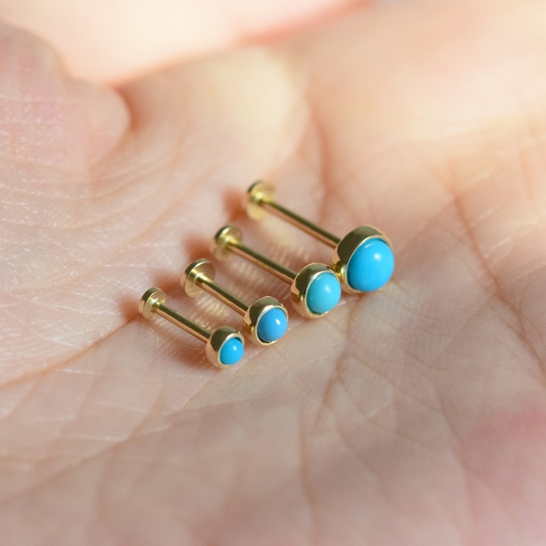 May include: Four gold body jewelry pieces with turquoise stones. The stones are different sizes, with the largest stone at the top of the image and the smallest stone at the bottom.