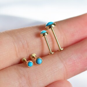 May include: Three gold body jewelry pieces with turquoise stones. The pieces are different sizes, with the largest piece on the left and the smallest piece on the right.