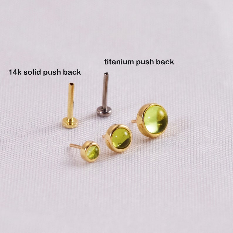 K&ouml;nnte beinhalten: Eine Sammlung von Ohrringen mit Gold- und Titan-Push-Back-Verschl&uuml;ssen und Peridot-Edelsteinen. Die Ohrringe sind in verschiedenen Gr&ouml;&szlig;en erh&auml;ltlich und tragen die Aufschrift "14k solid push back" und "titanium push back". Die Edelsteine sind hellgr&uuml;n.