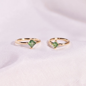 May include: Two gold hoop earrings with a square green gemstone in the center of each hoop.