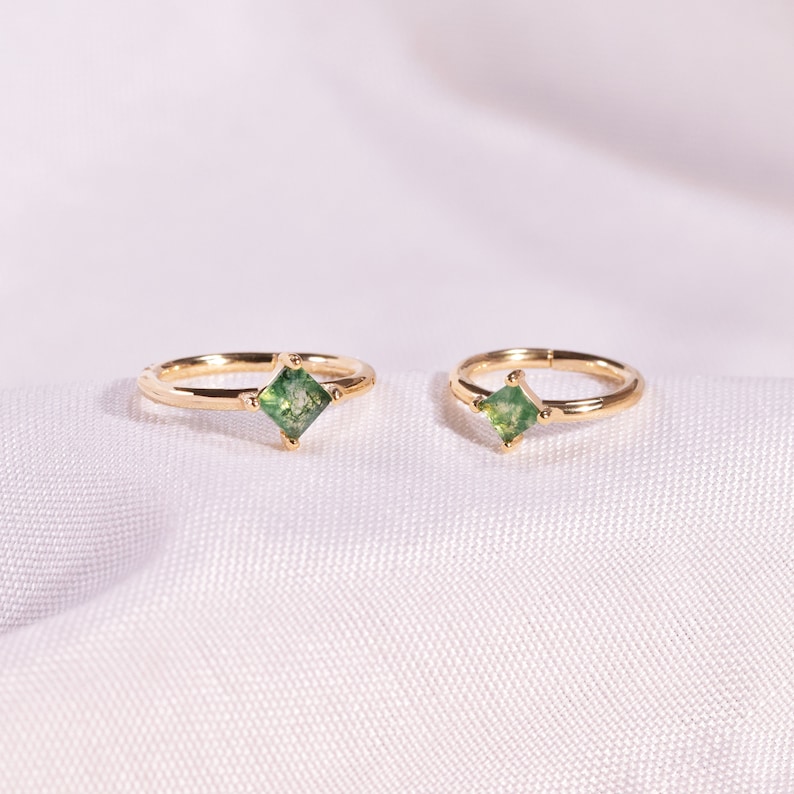 May include: Two gold hoop earrings with a square green gemstone in the center of each hoop.