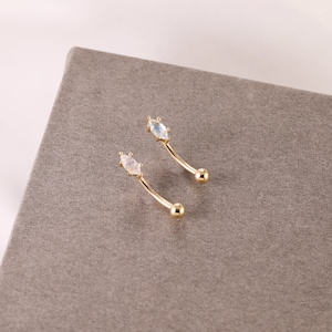 May include: Two gold belly button rings with clear and white marquise shaped gemstones.