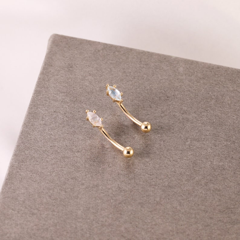 May include: Two gold belly button rings with clear and white marquise shaped gemstones.