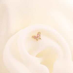 May include: A gold butterfly earring with pink and clear gemstones.