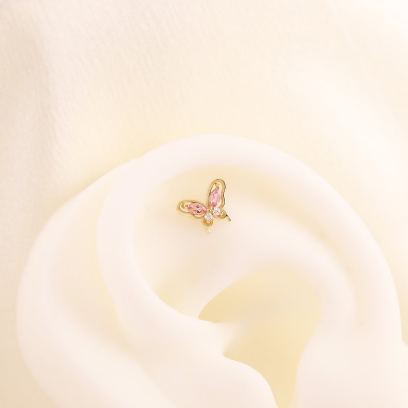 May include: A gold butterfly earring with pink and clear gemstones.