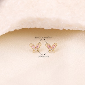 May include: A pair of gold butterfly earrings with pink tourmaline and clear moissanite stones.