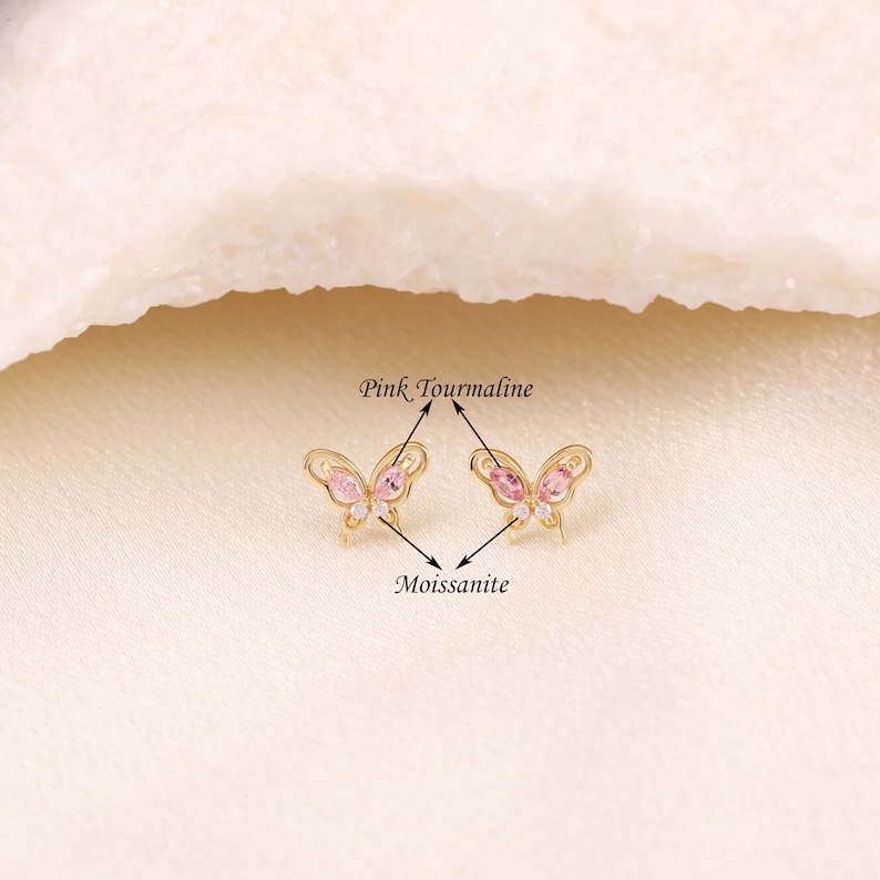 May include: A pair of gold butterfly earrings with pink tourmaline and clear moissanite stones.