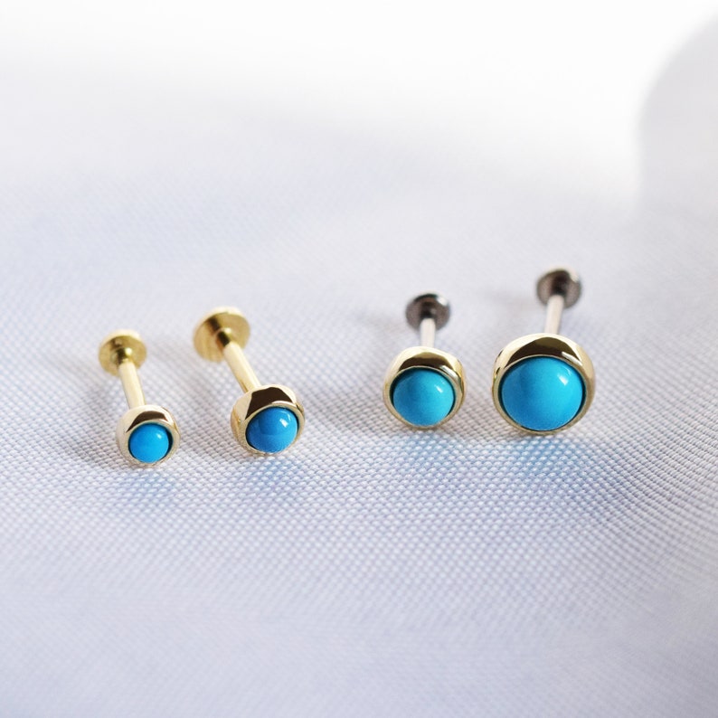 May include: Four gold body jewelry pieces with turquoise gemstones. The jewelry is in different sizes, with the largest piece on the right and the smallest piece on the left.