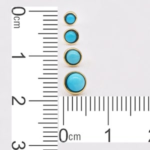 May include: Four turquoise cabochon gemstones set in gold settings. The gemstones are different sizes and are arranged in a vertical line. A ruler is visible in the background, with the gemstones measuring between 0.5 and 2 centimeters in diameter.