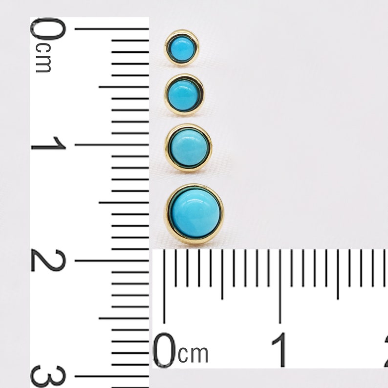 May include: Four turquoise cabochon gemstones set in gold settings. The gemstones are different sizes and are arranged in a vertical line. A ruler is visible in the background, with the gemstones measuring between 0.5 and 2 centimeters in diameter.