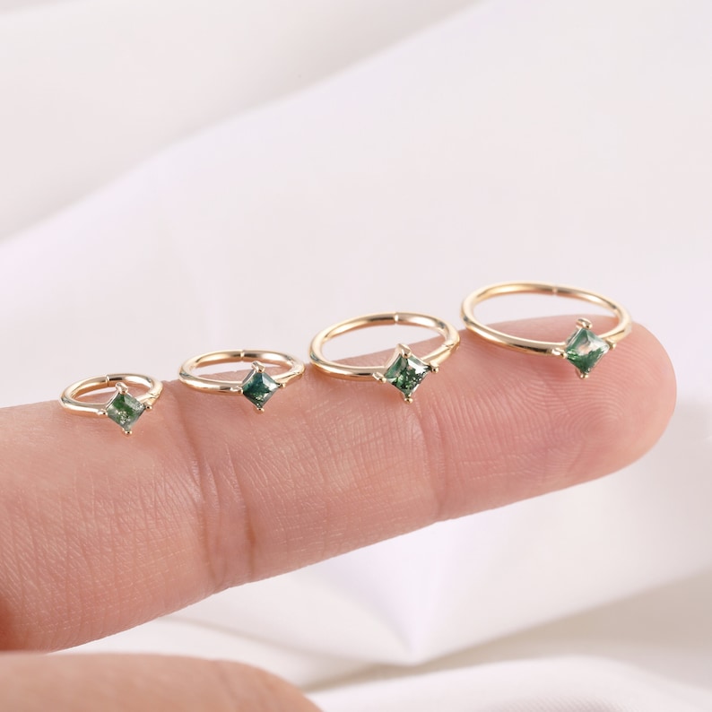 May include: Four gold hoop earrings with green square gemstones. The hoops are different sizes and are lined up from smallest to largest.