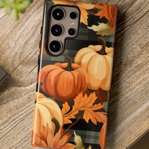 May include: A black and white plaid phone case with a fall theme. The case features orange and yellow pumpkins, brown leaves, and a camera cutout with a silver ring.