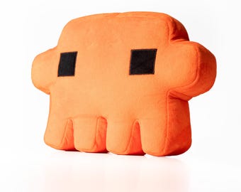 Peut inclure: Un coussin en peluche orange vif en forme de personnage stylisé avec une esthétique pixelisée et anguleuse. Le coussin présente deux yeux noirs carrés placés près du sommet et une base divisée en quatre sections distinctes et arrondies.