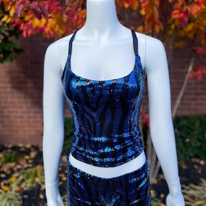 May include: A two-piece dance costume set on a mannequin. The set includes a tank top and shorts, both covered in blue and black sequins. The tank top has thin straps and a scoop neckline. The shorts are high-waisted.