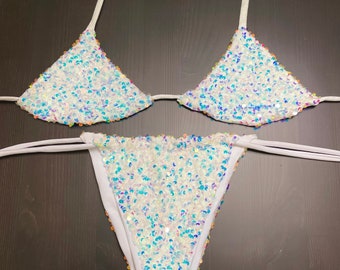 May include: A white bikini with iridescent sequins. The top is a triangle style and the bottom is a cheeky cut.