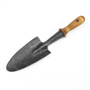 May include: A small, black metal hand trowel with a wooden handle. The handle is a light brown color and has a small black dot on the top.