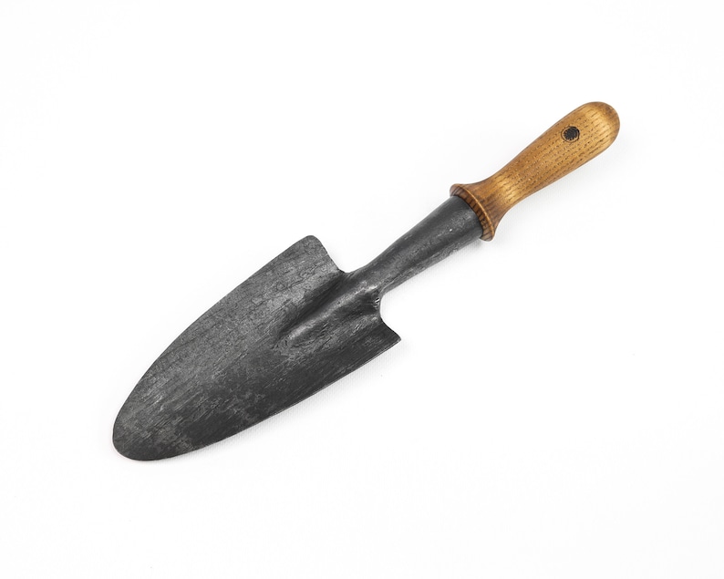 May include: A small, black metal hand trowel with a wooden handle. The handle is a light brown color and has a small black dot on the top.