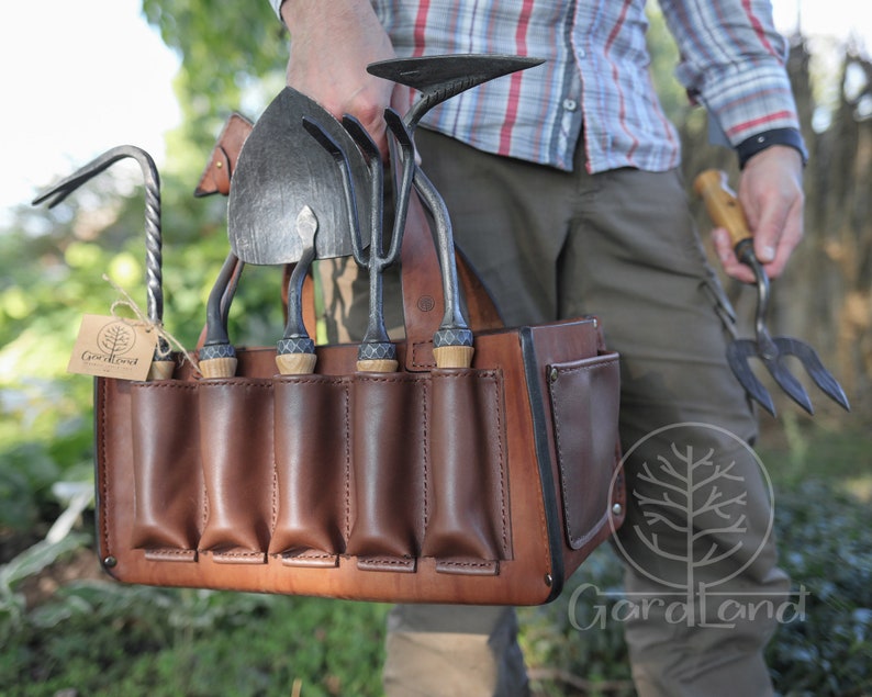 May include: A brown leather tool belt with multiple pockets for holding gardening tools. The belt is filled with various gardening tools, including a trowel, a hand rake, a cultivator, and a pruning shears. The belt is labeled "Gardaland".