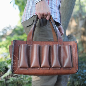 May include: A brown leather tote bag with five pockets on the front. The bag has a top handle and is made of a sturdy leather.