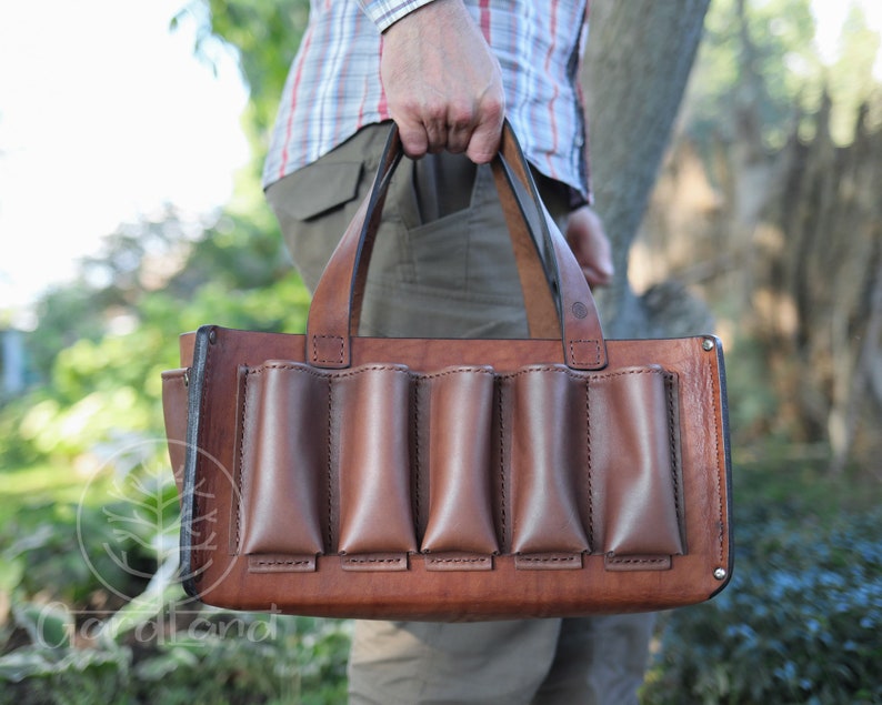 May include: A brown leather tote bag with five pockets on the front. The bag has a top handle and is made of a sturdy leather.
