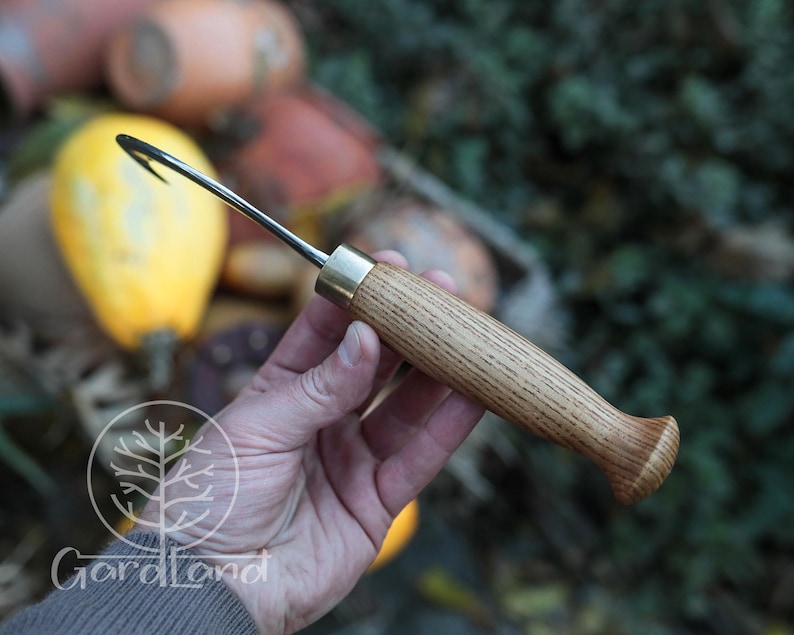 Puede incluir: Una herramienta de jard&iacute;n artesanal con un mango de madera y un gancho de metal curvado. El mango es de madera marr&oacute;n claro con una f&eacute;rula de lat&oacute;n. El gancho es negro y parece afilado. La herramienta est&aacute; dise&ntilde;ada para tareas de jardiner&iacute;a.