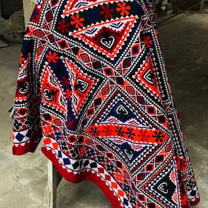 May include: A red, white, black, and blue patterned fabric with geometric designs. The fabric is folded and draped over a wooden stool.